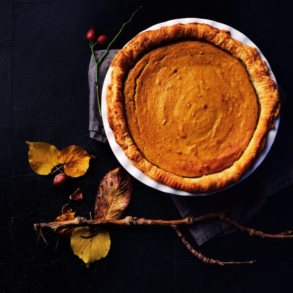 pumpkin pie sitting on a black tile with a grey napkin underneath and yellow leaves scattered around